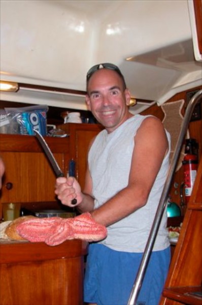 Scott in the galley of Honu, cutting warm bread; starfish potholder. 